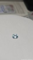 Close-up image of the natural aquamarine oval cut gemstone on a plain background showing its clarity and sky blue color.