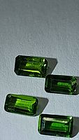 Four calibrated natural AAA grade Russian chrome diopside gemstones laid out on a surface, rectangular emerald cut, deep green color, showing clarity and color consistency.