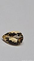 Close-up image of a pear-shaped natural golden citrine gemstone featuring facets and good clarity.