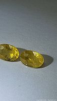Pair of natural canary yellow oval cut sapphires placed on a light-colored fabric background, showing gem facets and color.