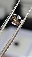 Close-up image of an oval faceted sapphire held in tweezers showing multicolored purple and green hues and facets on the surface