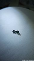 Two small oval sapphires placed on a white background, showing deep teal blue-green color and medium-dark tone under natural lighting.