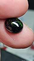 Close-up image of natural untreated jet black Ethiopian opal gemstone showing bright green and red flashes on a black base held between fingers.