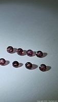 Eight round raspberry pink sapphires arranged in two rows on a white surface under light, showing facets and clarity.