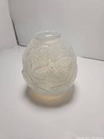 Front view showing round frosted glass vase with detailed butterfly and moth reliefs.