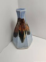 Hexagonal light blue glazed Mayhew pottery vase with dripping multicolor accents, narrow neck with flared top, approx 9x5x5 inches.