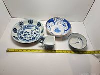 Photo showing the four pieces of blue and white pottery including plates, bowl, and jug with measuring tape as reference.