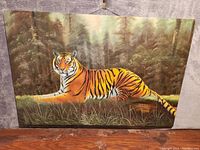 Front view of oil painting showing a tiger lying in grass with a forest background.
