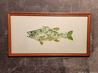Front view of framed fish painting showing greenish abstract fish on white background within wood frame.