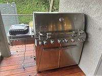 Stainless steel grill at left-front angle showing closed lid, side burner and control knobs