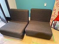 Two gray collapsible chairs side by side in seating position on basement floor.