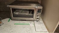Front view of stainless steel Breville toaster oven on countertop with instruction manual beside it
