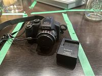 Camera body with attached lens cap, strap and charger on dark tabletop