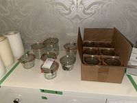 Nine Weck canning jars of various sizes displayed on a white surface, some with lids and clamps, next to a box containing unopened jars.