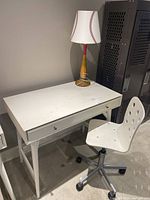 White desk with drawer, white office chair with caster wheels and circular cutouts, and baseball-themed lamp on top of desk, showing full set.