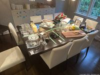 Set of 10 white upholstered dining chairs placed around a dark wooden dining table, showing the whole lot together.