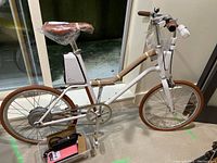 Full view of white folding Yunbike electric bike showing frame, saddle with plastic wrapping, handlebars, wheels