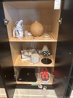 Cabinet interior with assorted essential oil diffusers, steamer, scale, and accessories arranged on three shelves.