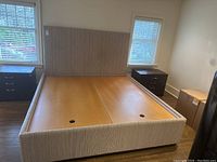 Full frontal view of the king size upholstered bed frame with headboard in a neutral beige fabric, showing wooden mattress support panels with circular cutouts.