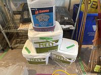 Four white buckets of environmentally-friendly ice melt stacked with 1-gallon container of Husky All Season windshield washer fluid on top.