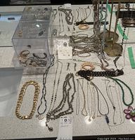 Wide view of assorted jewelry on white countertop showing necklaces, bracelets, and earrings including a flower-shaped brooch.