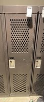 Front view of metal locker door with ventilation holes and locking handle.