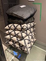 Stack of seven pillows showing two grey velvet pillows on top of five patterned cotton pillows with black geometric designs.