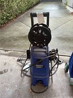Front view showing blue unit, hose reel, cords, and base wheels.