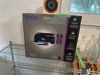 Front view of the Epson Expression Premium XP-620 printer in unopened box with a wooden speaker resting on top.