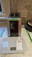 Revolution toaster with 'WORKING' label on top and Taylor kitchen scale in front on countertop.