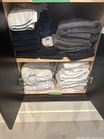 Shelves with neatly folded towels in black, gray, and lighter colors. Towels include different textures and some decorative edges.