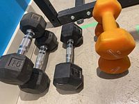 Photo showing two 15-pound black rubber hex dumbbells, one 12-pound black rubber hex dumbbell, and two 9-pound orange neoprene dumbbells on the floor.