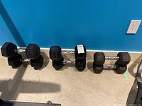 All six dumbbells (two each of 35 lb, 30 lb, 20 lb) lined up against blue wall