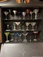 Full set of 25 martini glasses arranged on shelves in varied glass and metal styles