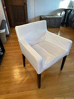 Side view of one white covered IKEA side chair showing the dark wood legs and fabric cover in a living room setting