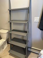 Front view of the slate grey wooden 5-shelf etager positioned next to a toilet, showing the shelf design and angled fronts.