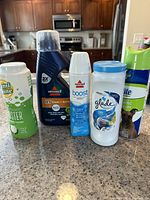 Front view of all five assorted cleaning products grouped on a counter including Lemi Shine booster, Bissell carpet cleaners, Glade air freshener and Nature's Miracle spray.