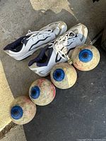 Photo showing four custom eyeball design candlepin bowling balls and a pair of white/navy bowling shoes.