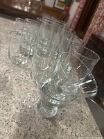 Photo showing multiple clear glass drinking glasses of various sizes arranged on a countertop including short wide glasses and taller cylindrical glasses.
