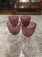Four purple wine glasses on a granite countertop, showing the full set and shape.