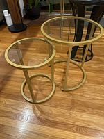 Two round gold tone metal frame nesting tables with glass tops on wooden floor
