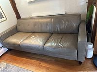 Front view of grey leather couch showing three seat cushions and button tufted backrest.