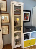 Front view of one white Billy bookcase showing glass door and interior contents