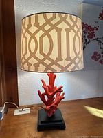 Front view of table lamp with coral base and cream patterned shade on black square pedestal.
