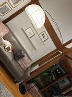 Full view of large arc floor lamp beside sofa, showing white paper lantern shade and black metal arching stand.