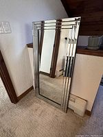 Front view showing the entire large rectangular mirror with three-layer mirrored frame leaning against a wall indoors.