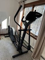 Side view of black Life Fitness elliptical trainer showing frame, pedals, handlebars, digital console and window light.