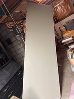 Full length view of the beige folding table held vertically, showing smooth tabletop surface and rounded corners.