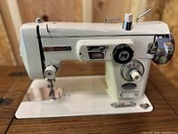 Close-up of white Morse sewing machine with various dials and controls, placed on a wooden surface.
