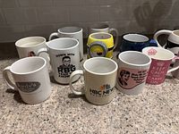 Multiple ceramic coffee mugs with various pop culture, media and motivational designs placed on countertop